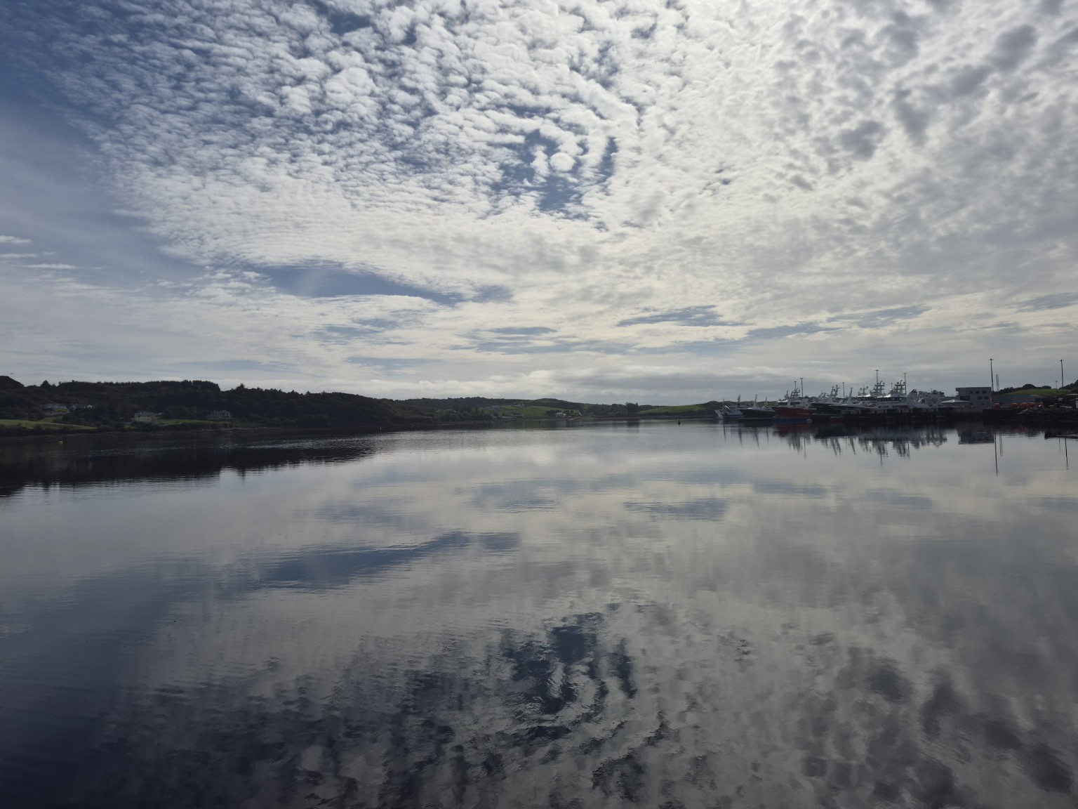 Fishing boats reflected in the calm water at Killybegs Harbour beneath a dramatic Donegal sky